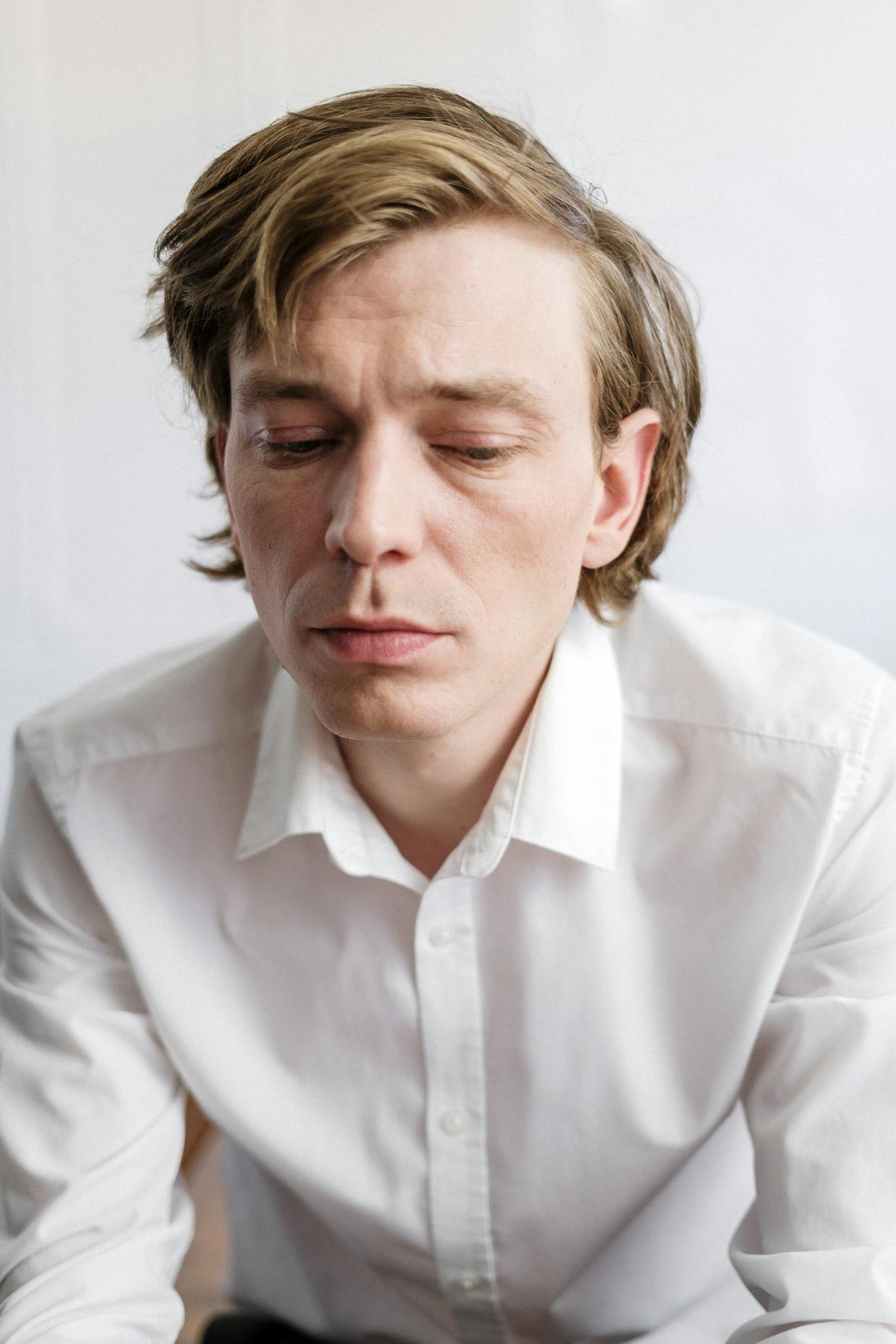 Close-up portrait of a pensive adult man in white shirt, conveying emotion.