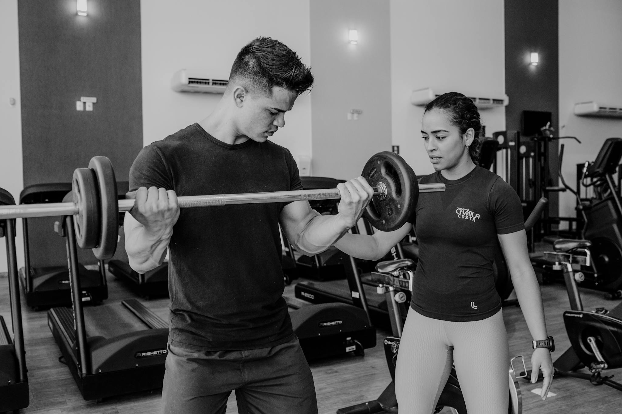Male athlete lifting weights with female trainer guidance in modern gym.